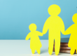 Yellow paper cut into the shape of a family of two adults and two children all holding hands