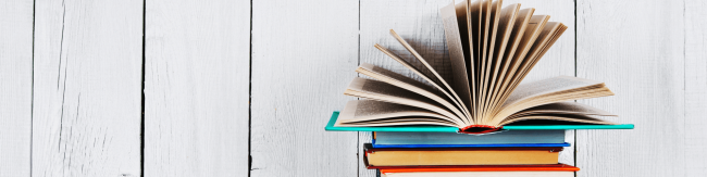 Colourful books stacked on top of eachother with the top book with open pages