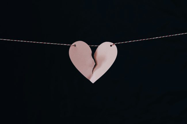 A pink paper heart hanging on a string with a rip down the center