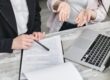 Two people sat at a table in front of a form and a laptop