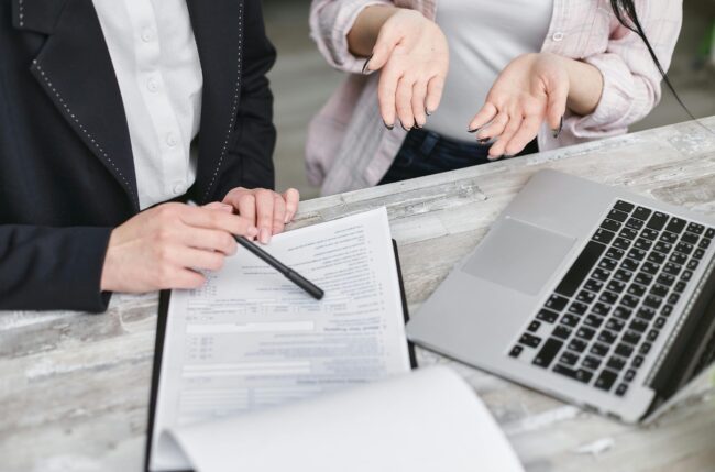 Two people sat at a table in front of a form and a laptop